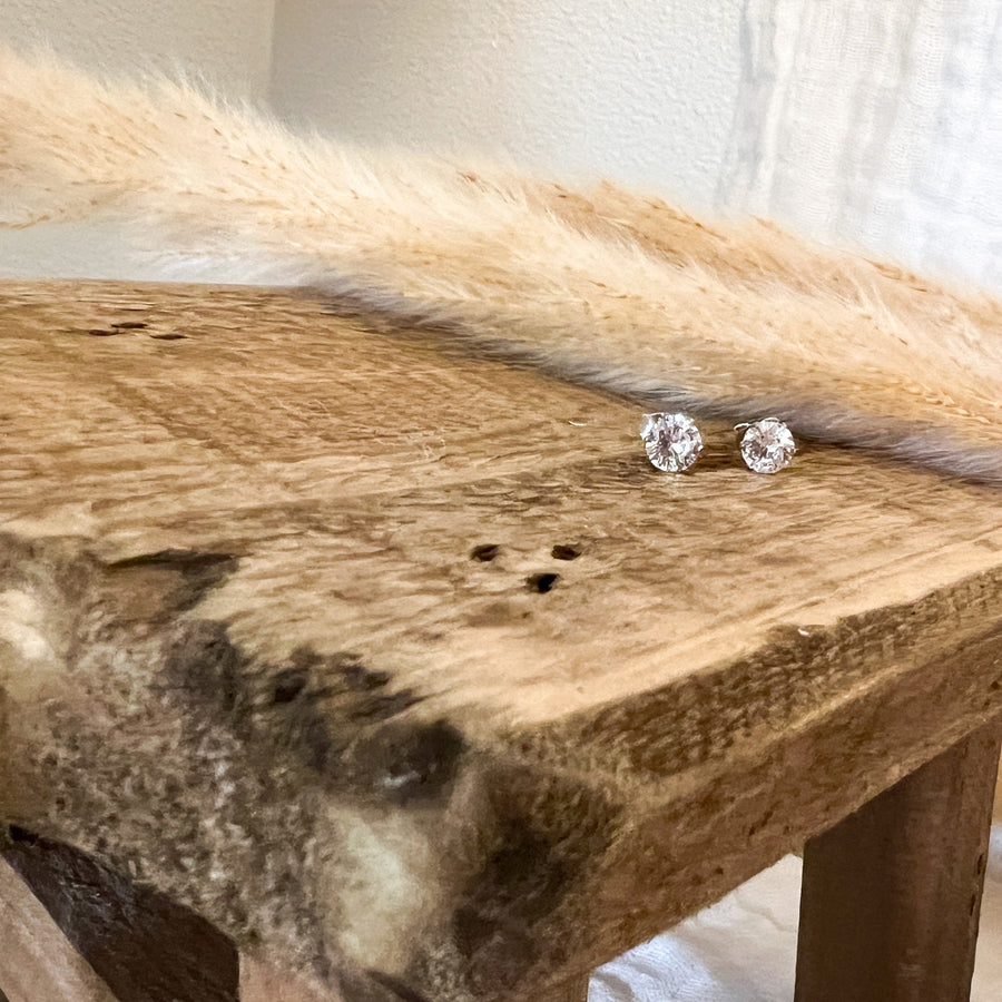 Pair of silver stud earrings on a wooden surface with dried grasses.