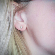 Close-up of an ear wearing a star-shaped earring with blonde hair.