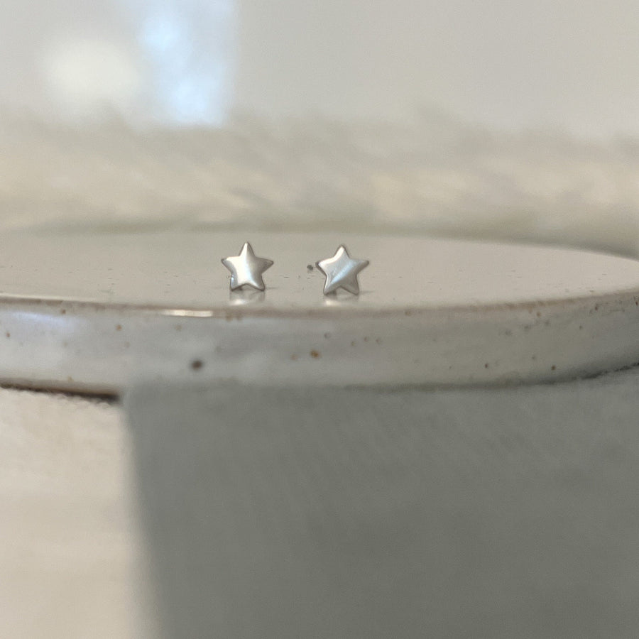 Silver star-shaped earrings on a neutral background